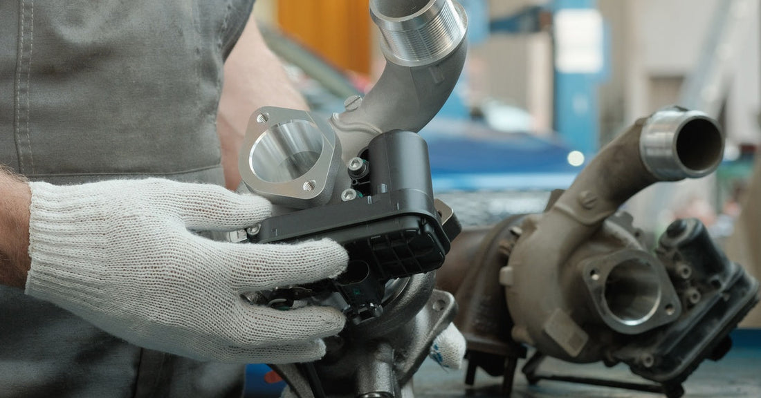  A mechanic holds a new turbocharger beside a worn unit on a workbench inside an automotive repair shop.
