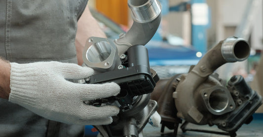  A mechanic holds a new turbocharger beside a worn unit on a workbench inside an automotive repair shop.