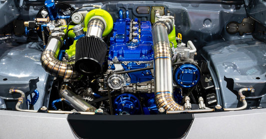 A modified diesel engine bay displays a bright green turbocharger beside a blue diesel engine and metal intake piping.