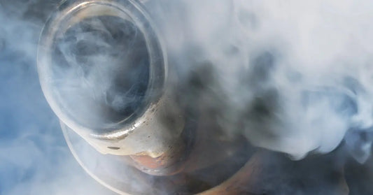 A close-up of the slightly rusty exhaust tip on a diesel vehicle, completely shrouded in hazy smoke.
