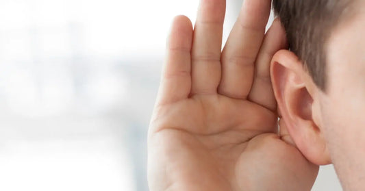 A close-up of a man cupping his hand behind his ear as if listening closely against a blurred background.