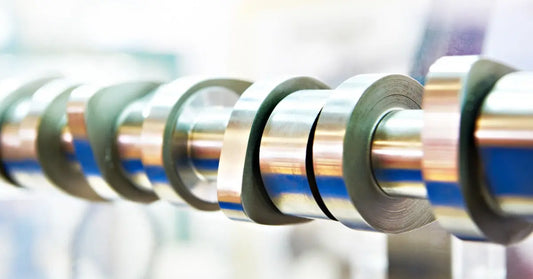 A close-up of a polished camshaft showing offset lobes and journals lined up along the steel shaft.