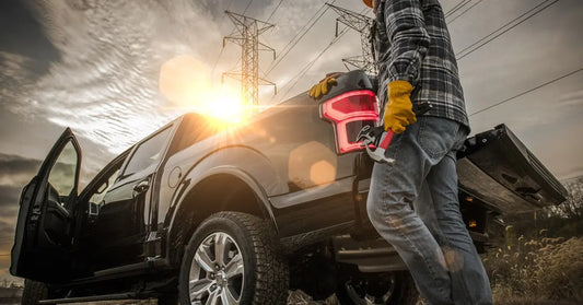 A blue-collar man standing by the tailgate of his big black pickup truck. The sun shines down on them.