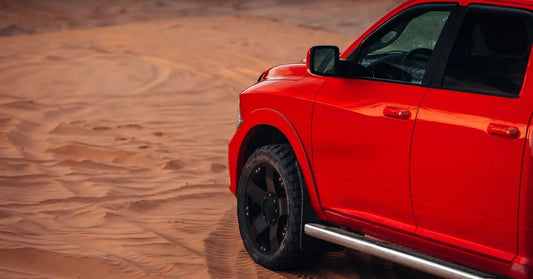 A large red truck driving through the desert. The sand is full of visible tire tracks going in multiple directions.