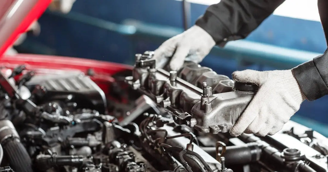 A pair of white-gloved hands lowering a component of a diesel engine into the bay of a red pickup truck.