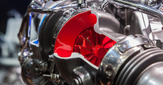 A cutaway turbocharger reveals a bright red compressor wheel among polished pipes and silver metal housings.